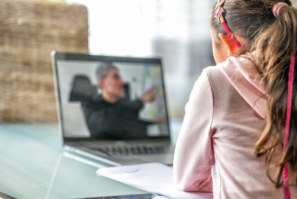 Learner studying online with her teacher visible on her laptop screen