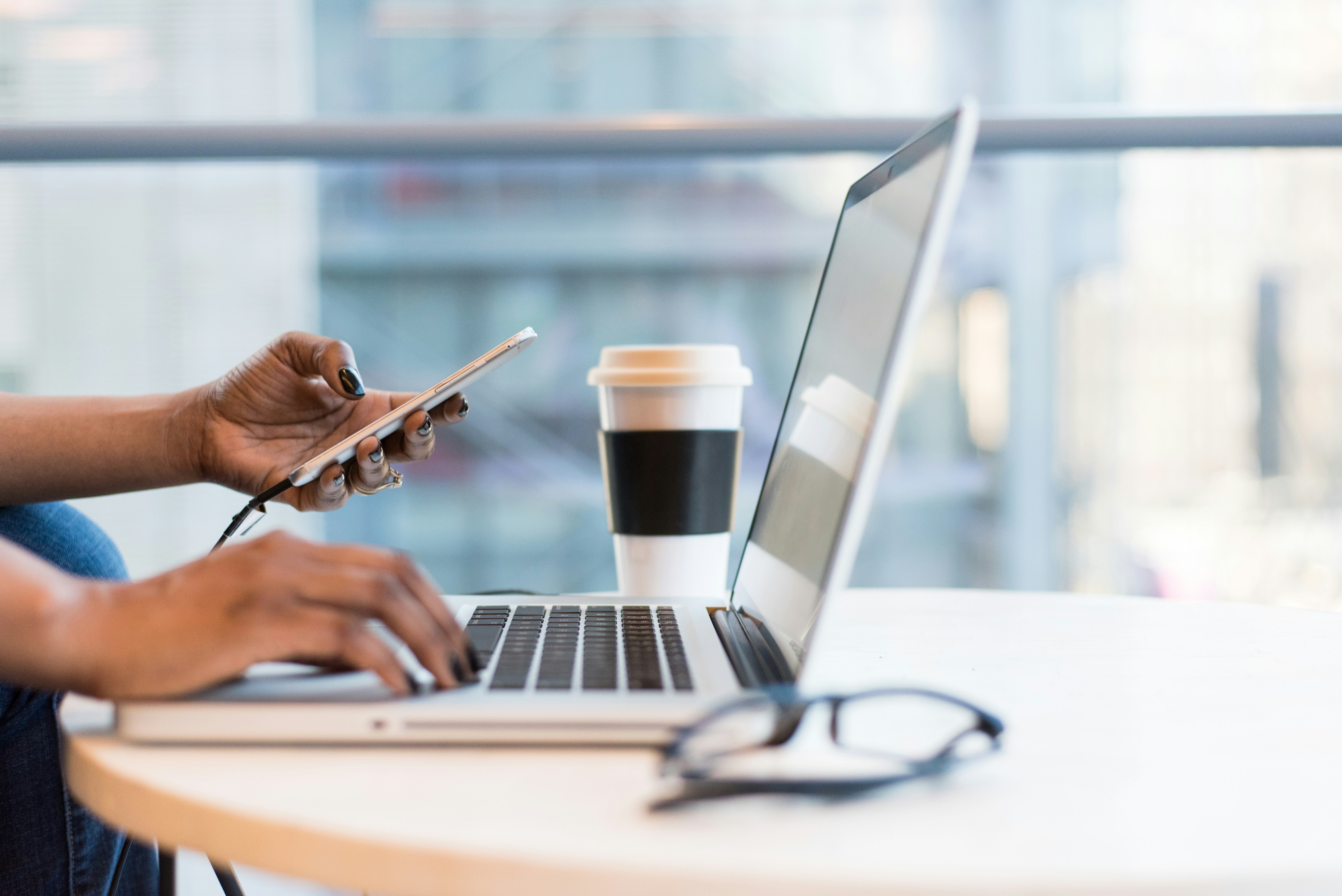 Close up of person using a laptop while looking at their mobile phone.