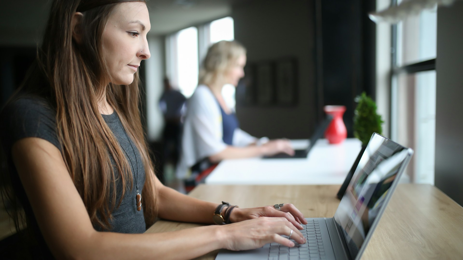 Woman sat at a shared desk, typing on a laptop.